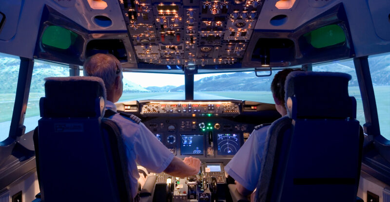 Two pilots are sitting in the cockpit of a smaller aircraft