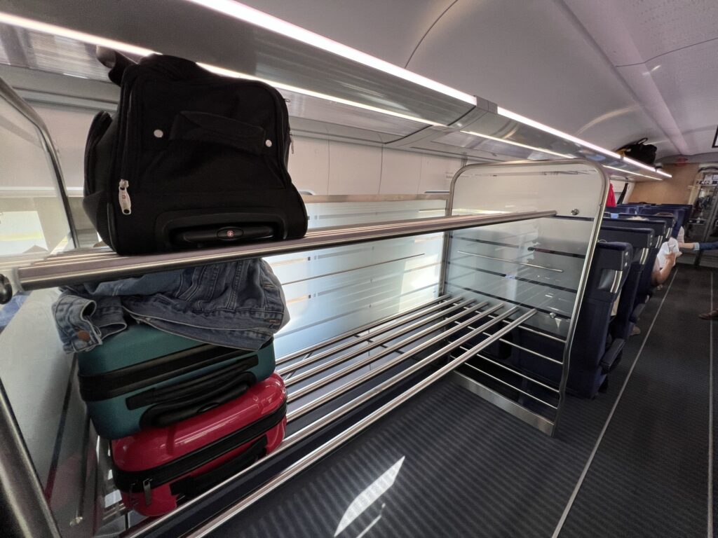 A dedicated bag storage area on DB’s Deutsche Bahn InterCity Express (ICE) between Hamburg and Berlin. A few suitcases are in view on the rack. There is also a smaller overhead bin in view.