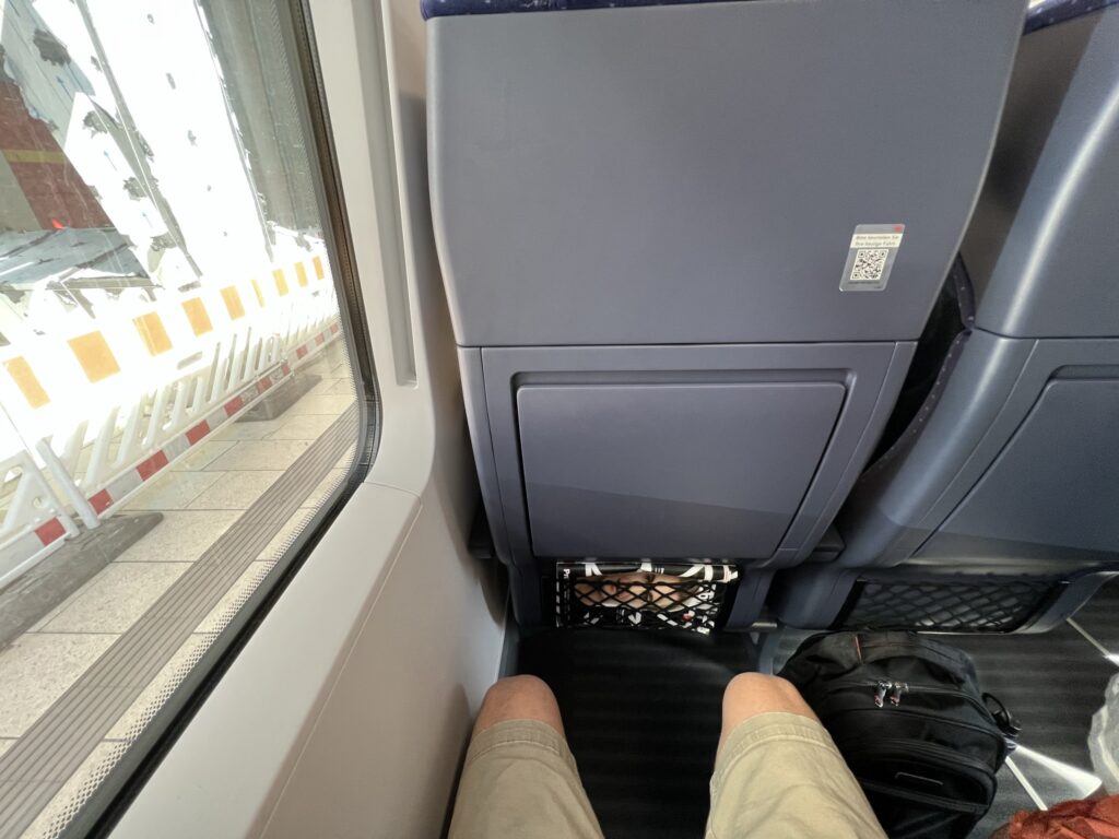 A man's knees are showing a large amount of space between him and the seat in front of him.