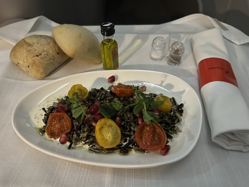 A large salad with side rolls sitting atop the business class tray table