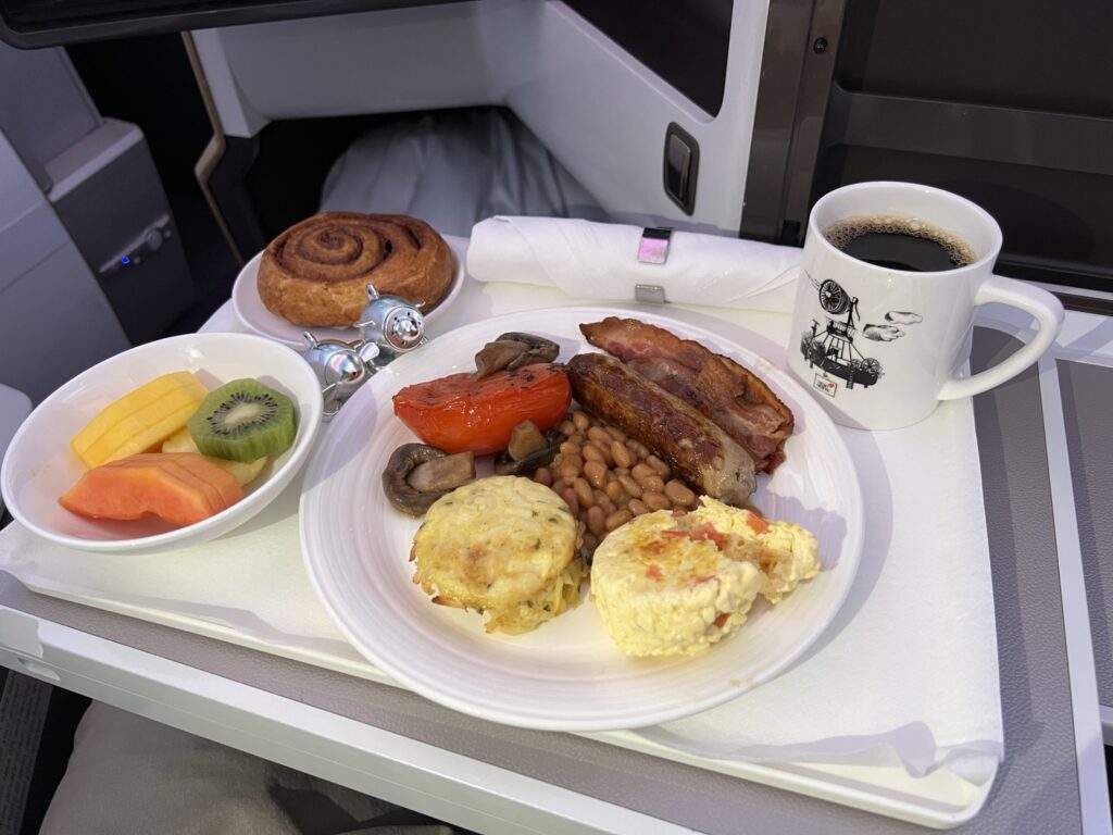 with eggs, sausage, tomato, mushrooms, beans, fruit and cinnamon roll served in Virgin Atlantic's Upper Class suite.