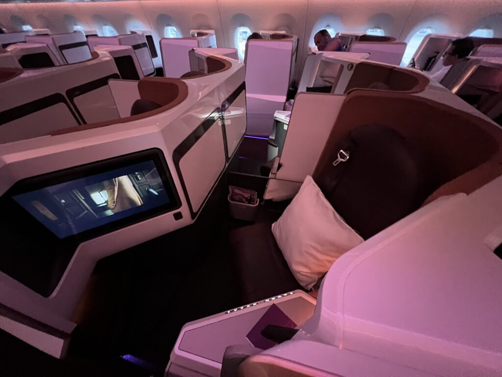 The Upper Class suite onboard the Virgin Atlantic A350-1000, with a focus on the brown seat surrounded by polished thermoplastics with pink LED lights casting an interesting glow