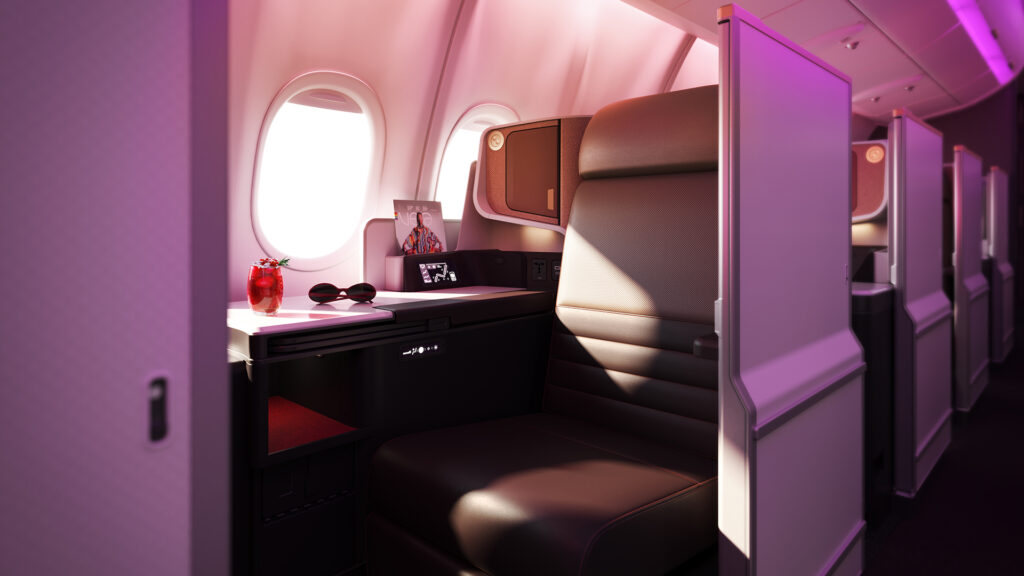 Virgin Atlantic business class suite is pictured here next to the aircraft window. The seat is brown with red accents around.