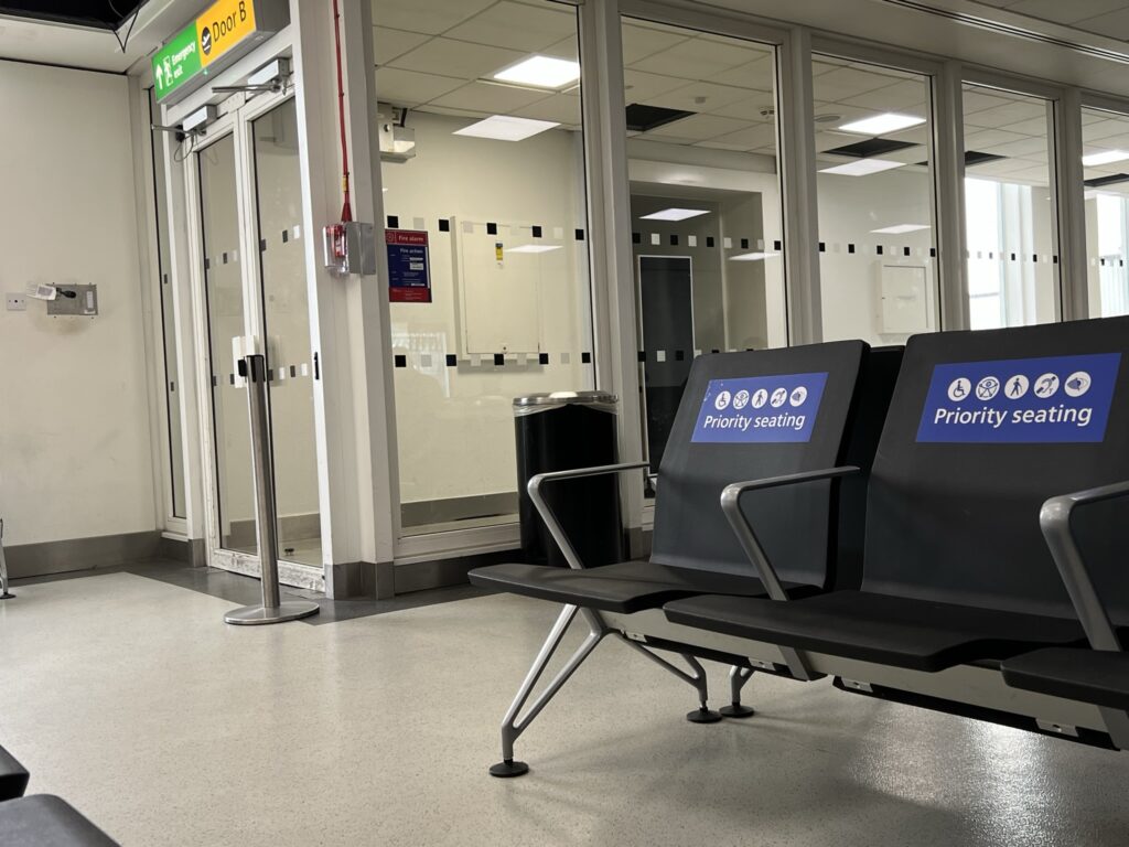 A hold area at London Heathrow, with a couple of seats in view listed as 'priority seating' for PRMs and others in need of a physical seat