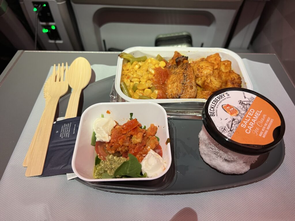 A chicken dish with potatoes and corn, a salad, ice cream and wooden utensils. The ice cream carton has frost on the outside 