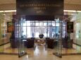 A large glass entry way into the Albany International Airport reading lounge. A sign above the entry way says "The Mario and Matilda Cuomo Pavilion"
