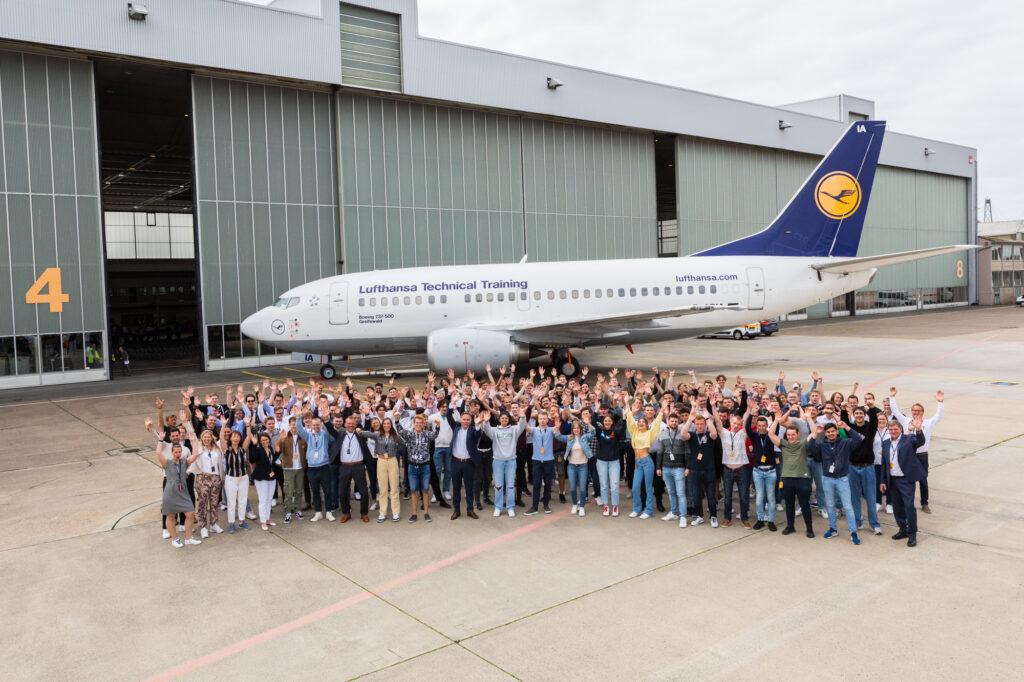 A large group of people in training stand in front of a Lufthansa aircraft