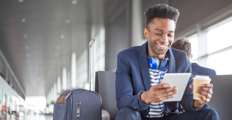 Young man with headphones and coffee waiting at the airport lounge and using a tablet Conetic