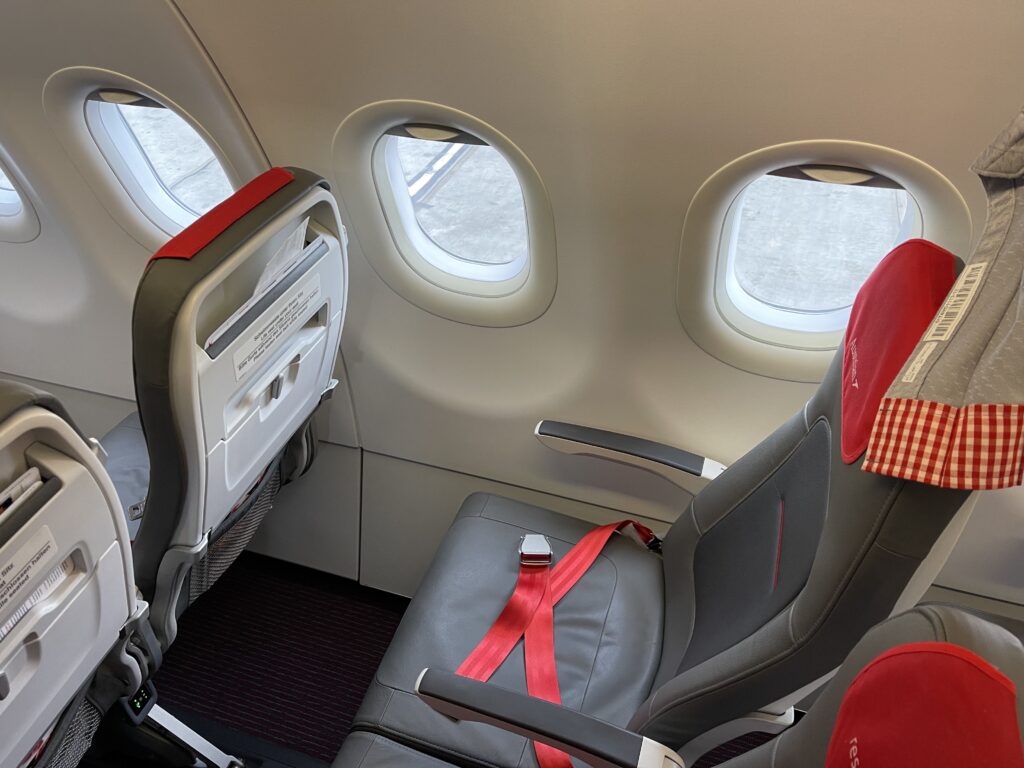 Austrian Essenza seat is grey with a red headrest cover and red seatbelt. 