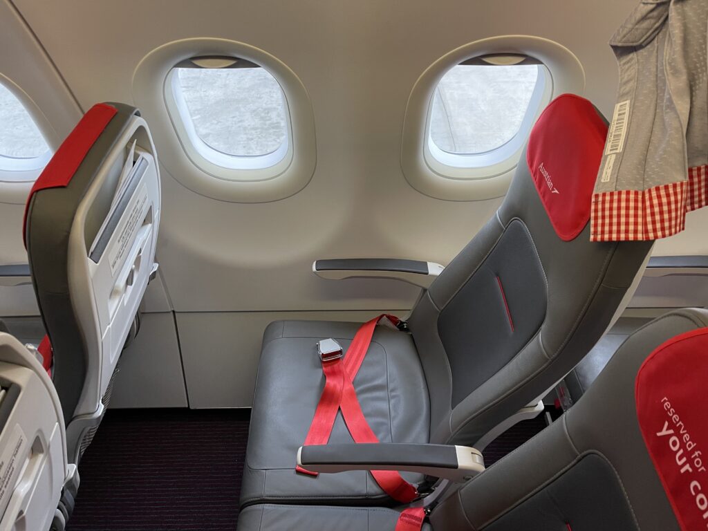 Austrian Essenza seat is grey with a red headrest cover and red seatbelt. This photo shows the slimline nature of the seat.