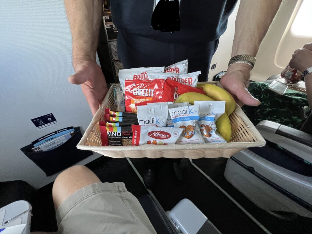 A flight attendant is offering a selection of snacks to a passenger.