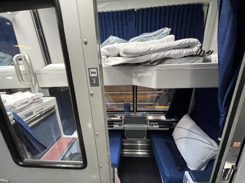 Looking into the Amtrak Roomette with the upper bed pulled out, and bedding atop it