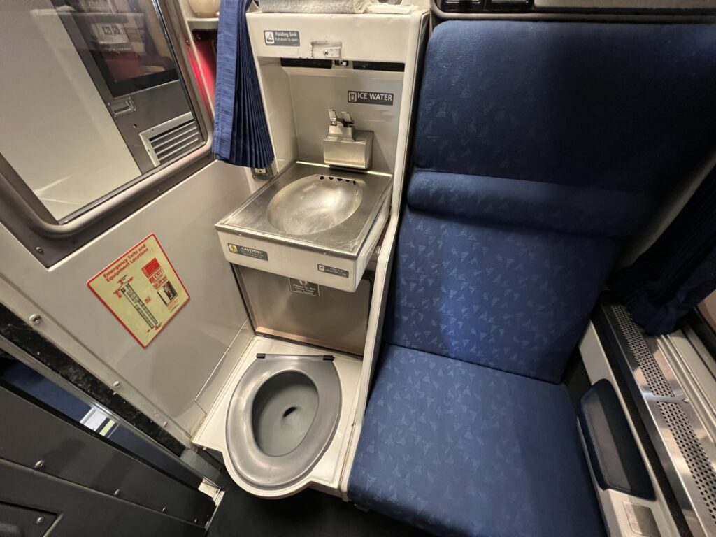 A toilet and sink are seen next to the seat in the Amtrak Roomette