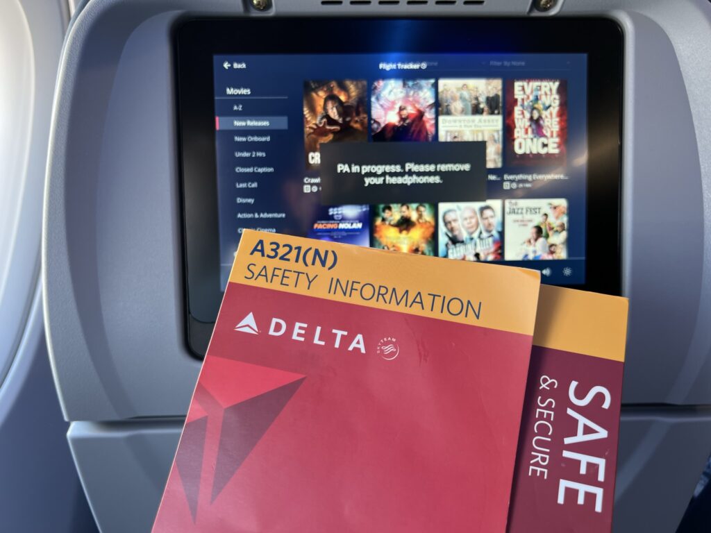 A safety card is being held up in front of the Delta A321neo embedded IFE screen.