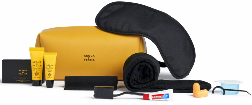 Air Canada Acqua di Parma Amenity Kit is displayed with its contents. The kit is a peachy orange colour. There is a mask, two small bottles, ear plus, tooth brush and tooth paste.