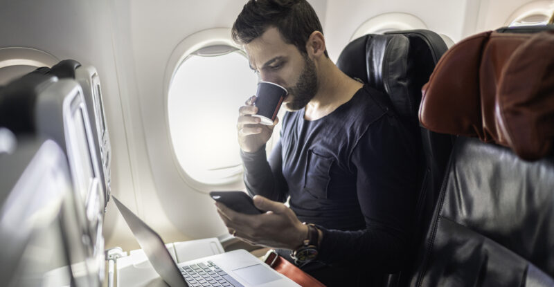 Man working in airplane using cellphone and drinking coffee