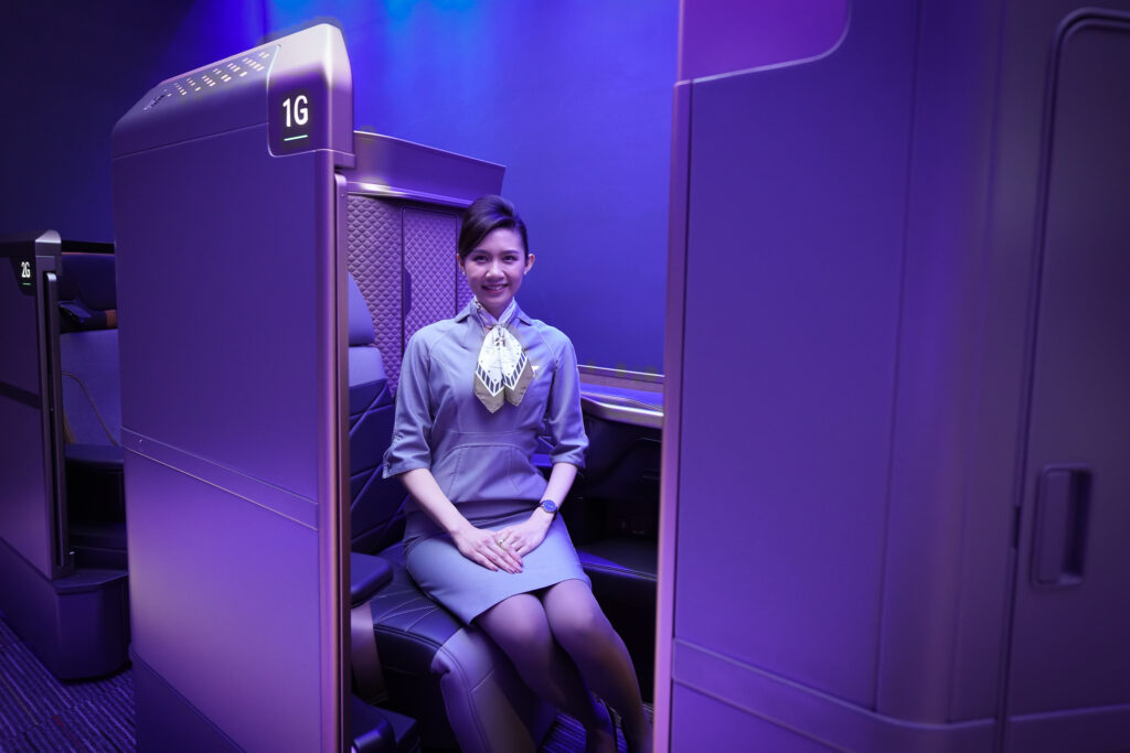 A female crew member is sitting in the first class seat on the A350. This images exemplifies how tall are the doors in first class.