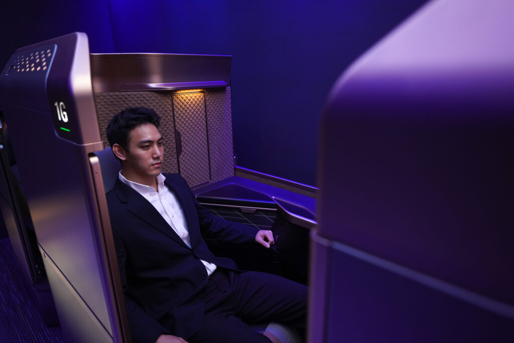 A man in a suit is sitting in the Starlux first class A350 suite. Purple and blue lights cascade around the seat.