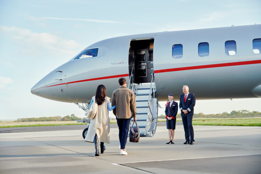 A man and women are walking towards a VistaJet aircraft for boarding.