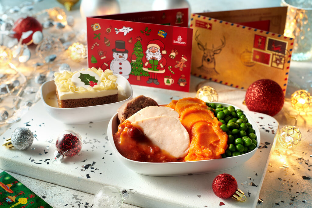 Emirates' Christmas menu dinner in economy, accompanied by Christmas cake and surrounded by festive cards and décor.