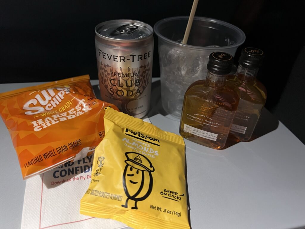 Snacks, club soda and a couple of bottles of Woodford Reserves are displayed on the tray table