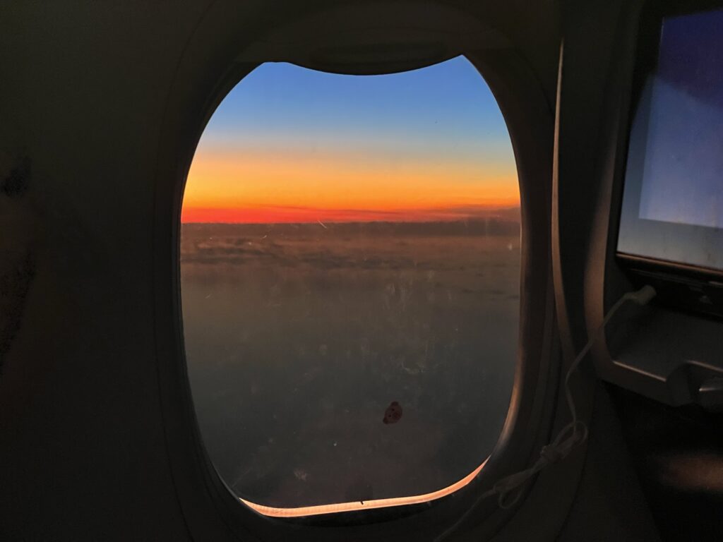 A photo of sunset and clouds outside the author's aircraft window. Blue, orange and red can be seen in the sky.