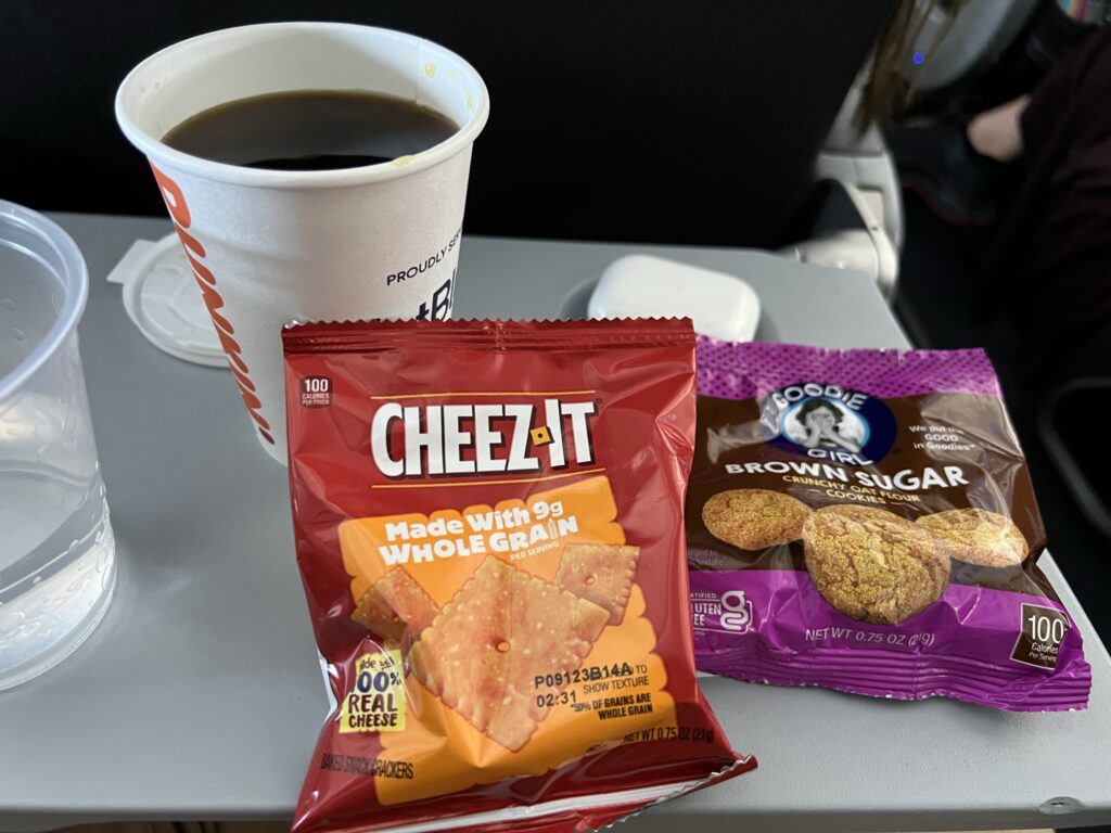 A variety of snacks onboard the JetBlue tray table, plus a cup of coffee 