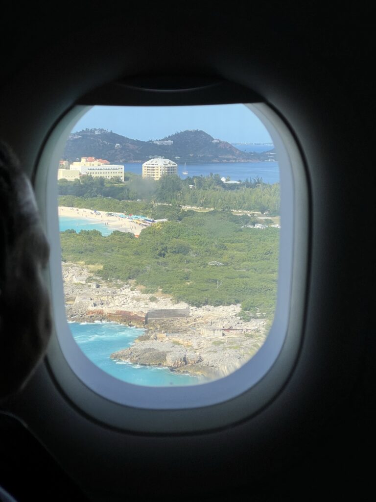 A photo out the window of the aircraft showing beautiful St. Maarten, including blue ocean and lots of greenery