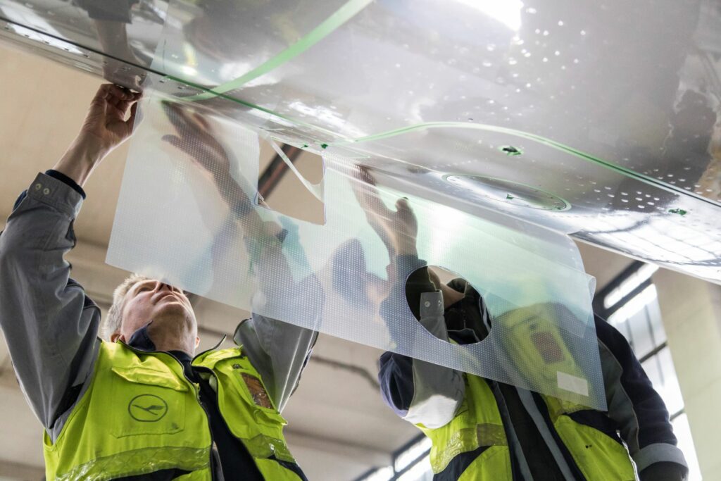 An employee is applying the Sharkskin technology to a Lufthansa aircraft.