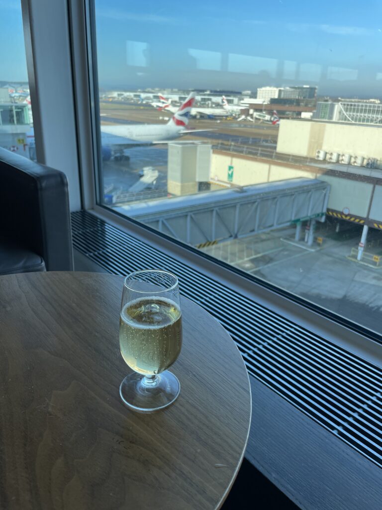 A glass of Champagne sitting on a table in the lounge. The tails of parked BA aircraft can be seen through the window.