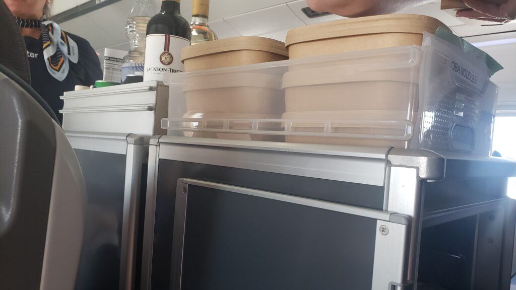 A trolley is pushed down the aisle during the meal service. It is loaded with snack boxes and meal boxes.