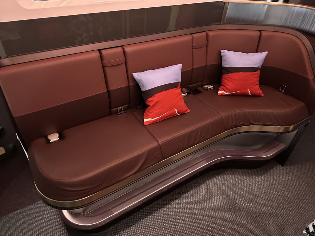 Virgin Atlantic's Loft. A long bench in brown leathers with red throw pillows.