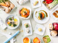 An assortment of Korean vegan dishes are displayed on white plates. A small toy plane is in the bottom corner of the display.