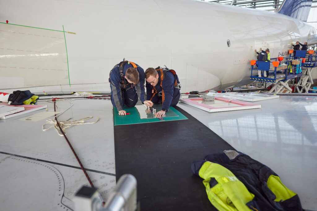 Two men are trimming the AeroSHARK layer in preparation for application. 