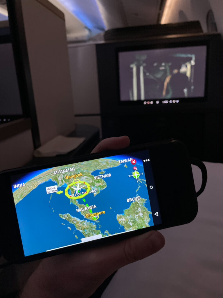 A tethered remote is being held up in front of the IFE screen. It is showing the 3D map, while the IFE screen is playing a movie.