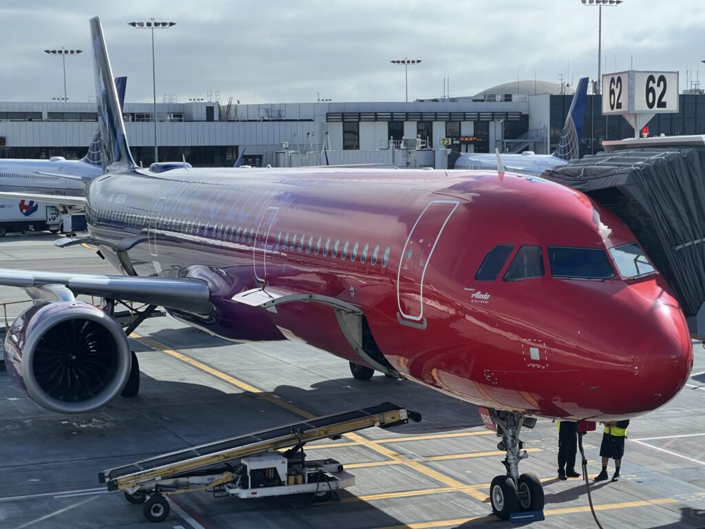 Alaska's Airbus A321neo with red livery is parked at the gate of LAX.