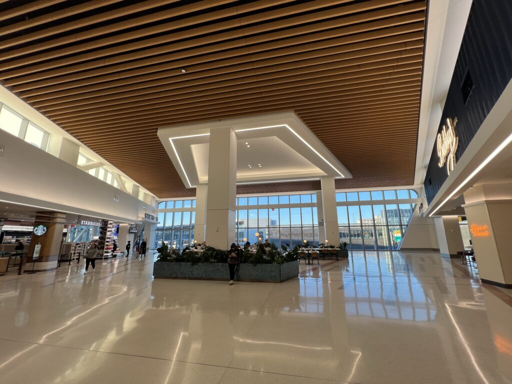 LaGuardia food hall has high ceilings and floor-to-ceiling windows. A Starbucks is tucked in theh corner.