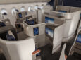 Rendering of Lufthansa Allegris business class cabin on display. The seat is rich blues with white thermoplastics and a few faux wood detailing.