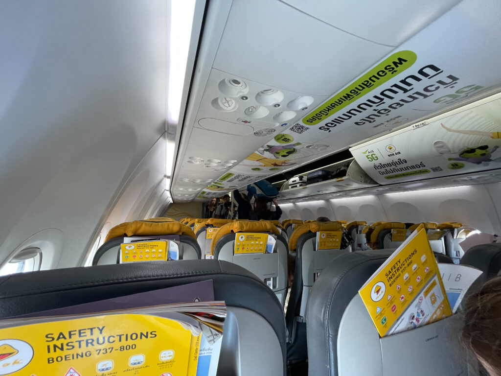 A photo from the rear of the aircraft showing rows of seats in front of the author, and their literature pockets stuffed with safety info and the inflight magazine. 