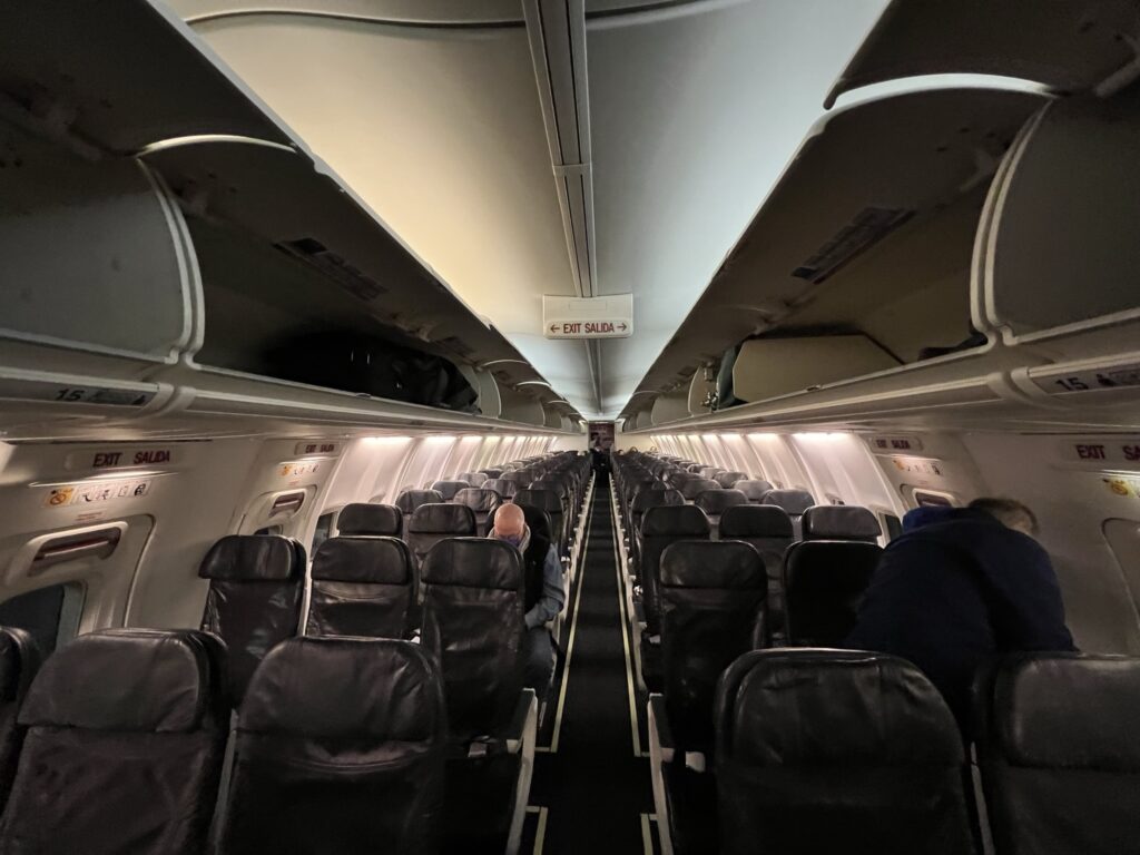 Cabin interior of a Boeing 737-800. Overhead bins are open for boarding. The interior looks worn.