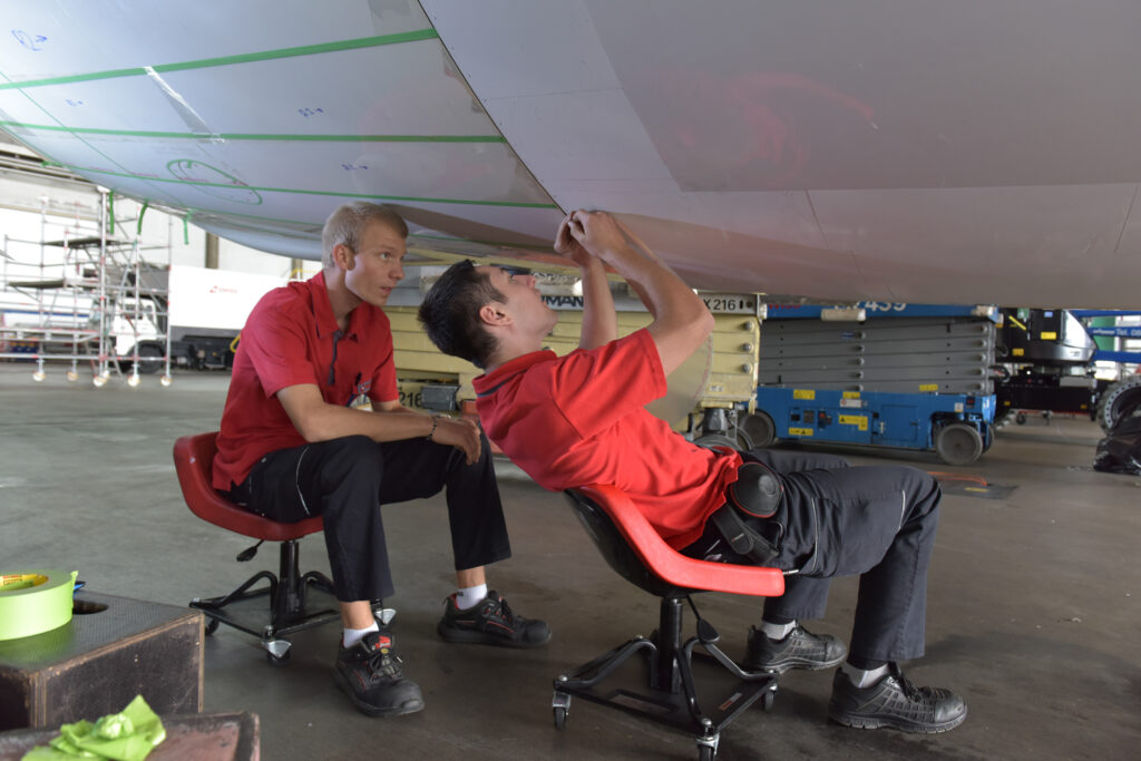 Two men are applying the AeroSHARK layer to the belly of an aircraft.