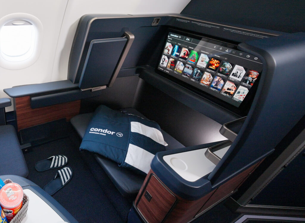 Business class seat for Condor is in deep blues with dark wood accents and a large IFE screen.