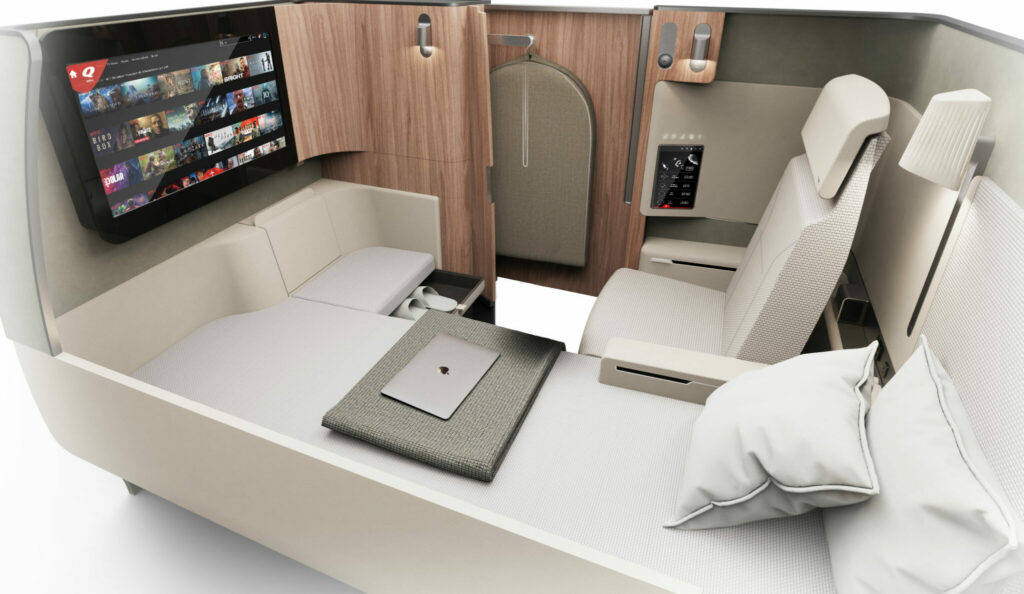 Qantas' Project Sunrise A350 first class suite. White and cream fabrics for the seat and bed with light wood finishes around the suite. The IFE screen is seen in this image, and can be viewed whilst a passenger is in bed or seated.