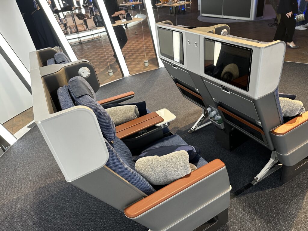 A view over top of the Allegris premium economy seat shows grey thermoplastics, navyseat covers and wood-like details.