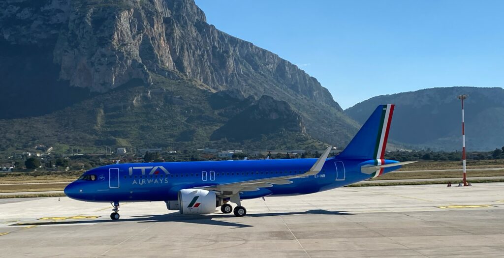 ITA Airways A320neo delivered in February 2023 fitted with Iris compatible satellite communications. The aircraft is covered with blue livery. A mountainous view is in the background.