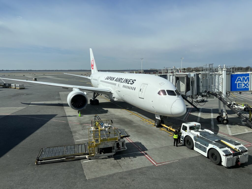 JAL 787 parked at the gate on a sunny day, waiting for passengers to board.