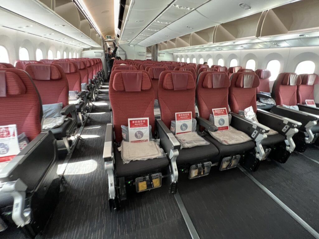 JAL economy class cabin. The wide seats are red on top and grey on the seat bottom.