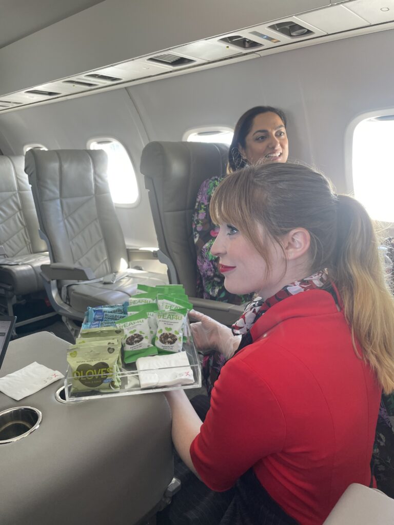 A flight attendant is showing a tray of various premium snacks such as nut mixes and olives. 