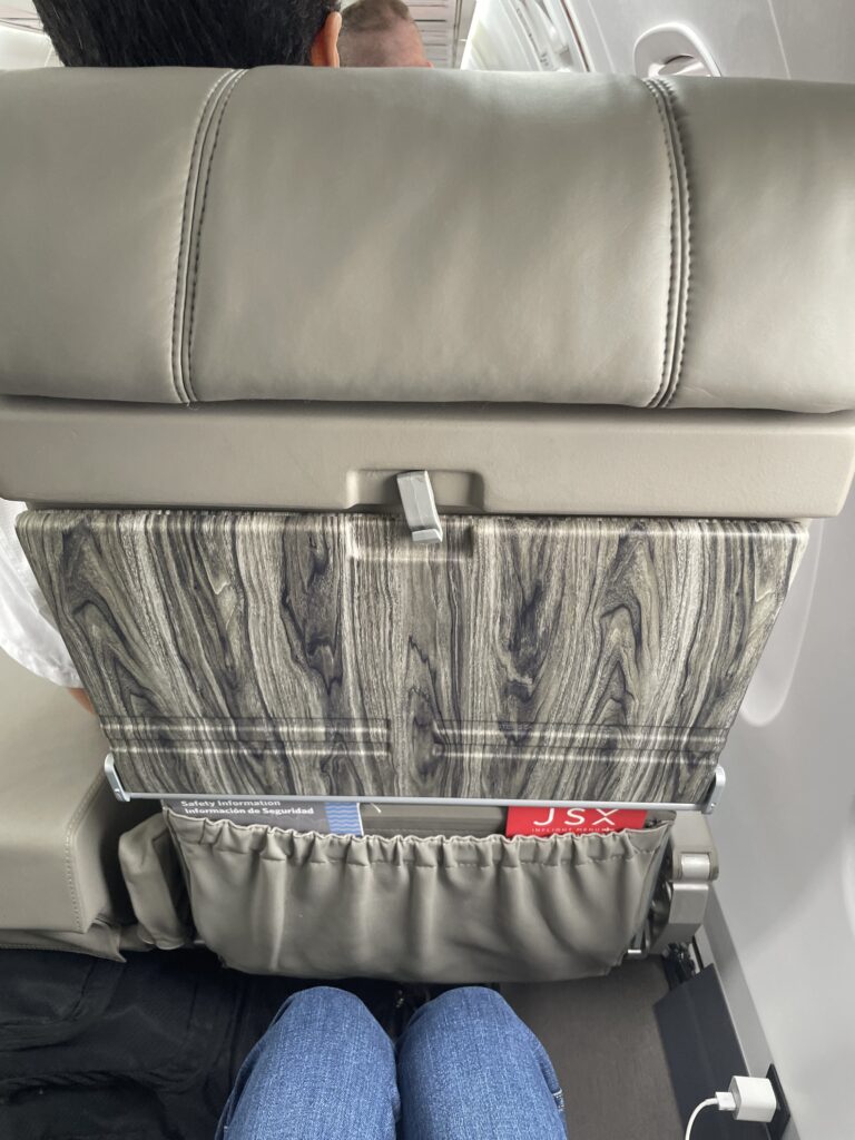 A wood-like effect is seen on the tray table. The author's knees are also in view, and clearly a few inches away from the seatback in front of her.