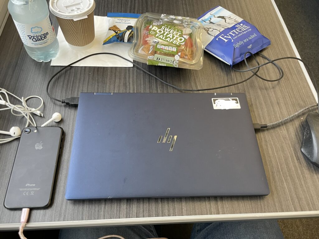 A laptop sits on a train table with some snacks and a coffee sitting behind it.